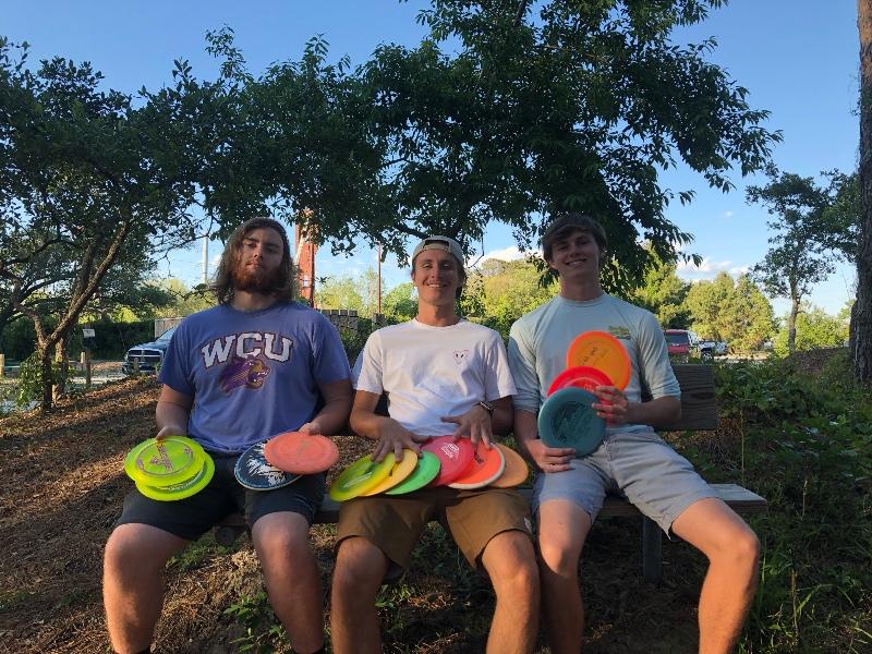 Seniors (from left) Cameron Liston, McCabe Owens and Brady Van Lunen pose for a photo holding their discs after playing a game of disc golf on the Casey R. Logan Disc Golf Course. PHOTO BY KATIE MACBRIDE/Nighthawk News