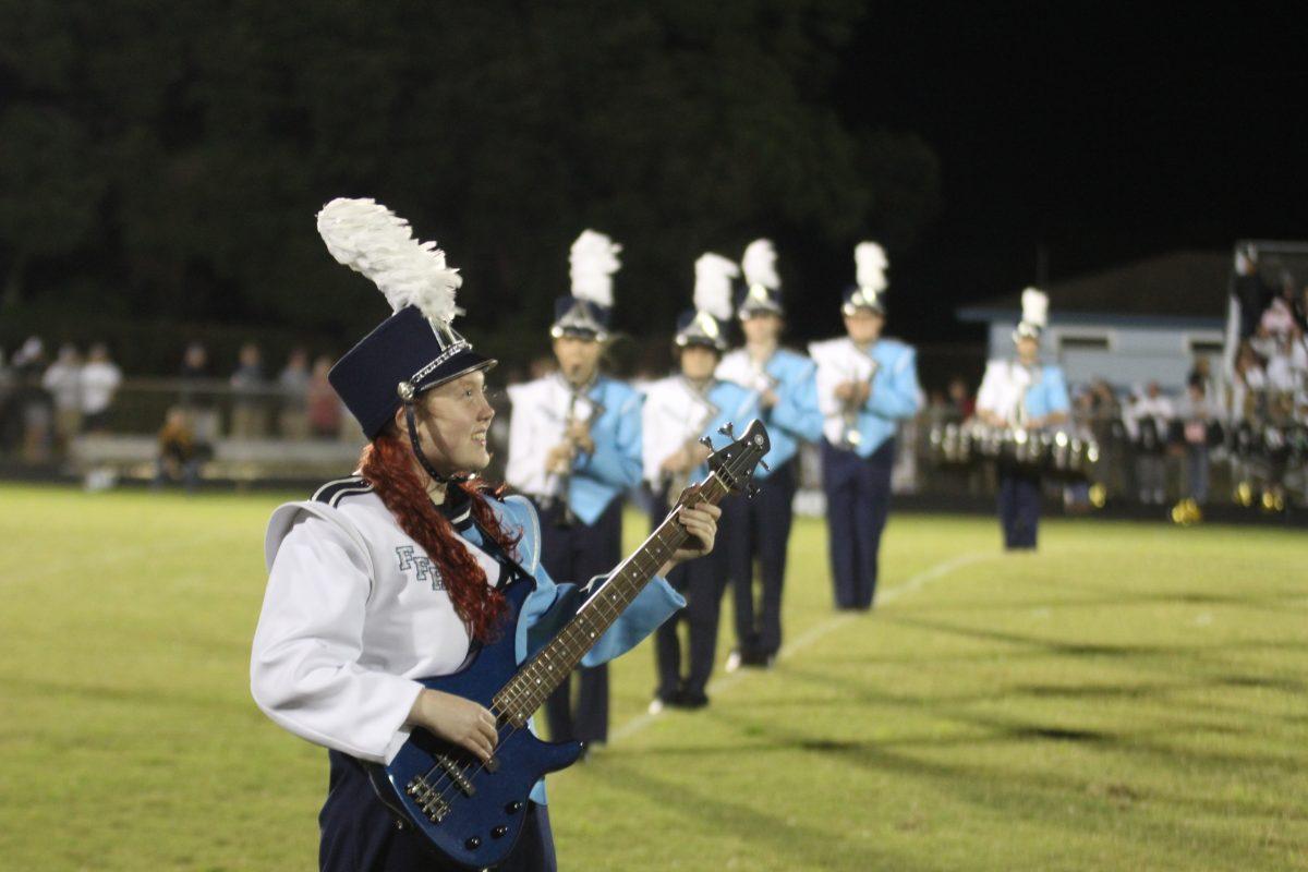 Junior Delaney Hanf strums the bass guitar at a football game.