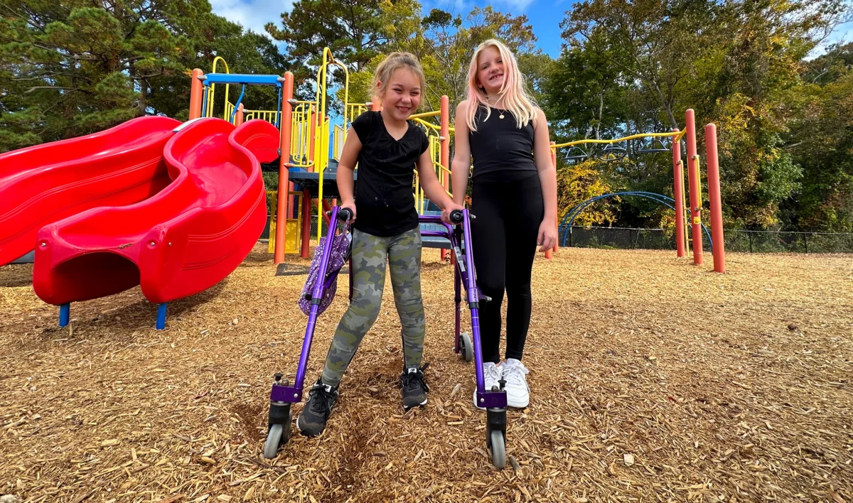 Friends Nola Flock (left) and Penny Krieg smile in front of the Kitty Hawk Elementary School playground. The KHES Playground Project hopes to lead to more inclusive fun, with fundraising efforts underway for a new facility.
Submitted Photo